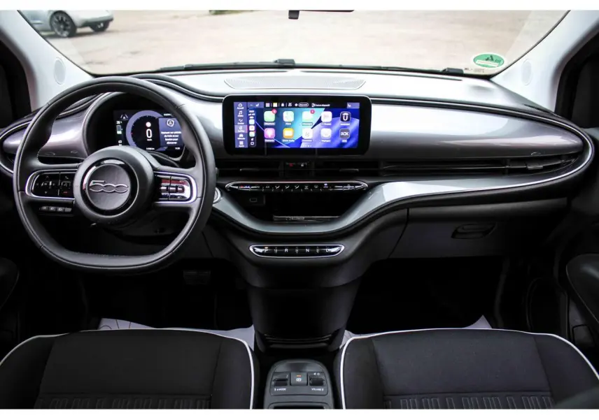 Vue intérieure frontale du tableau de bord noir de la Fiat 500 électrique 2023 avec écran tactile central et volant multifonction.