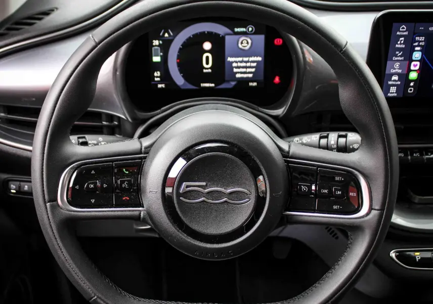 Vue rapprochée du volant noir de la Fiat 500 électrique 2023 avec commandes intégrées et tableau de bord numérique.