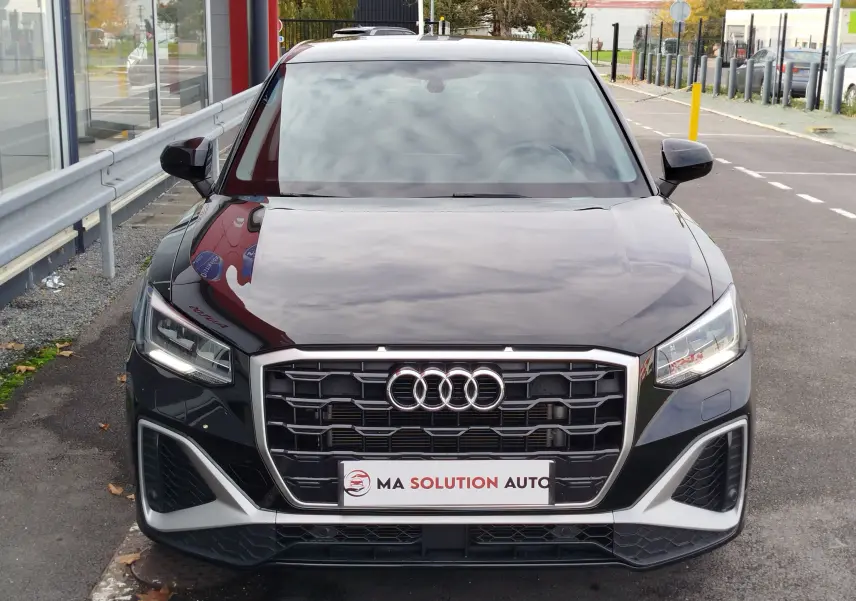 Vue de face d'un Audi Q2 noir mito metal 2023 avec calandre hexagonale et phares LED allumés.