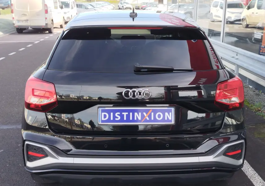 Vue arrière d'un Audi Q2 noir mito metal 2023 avec feux rouges et logo Audi bien visibles, stationné en extérieur.