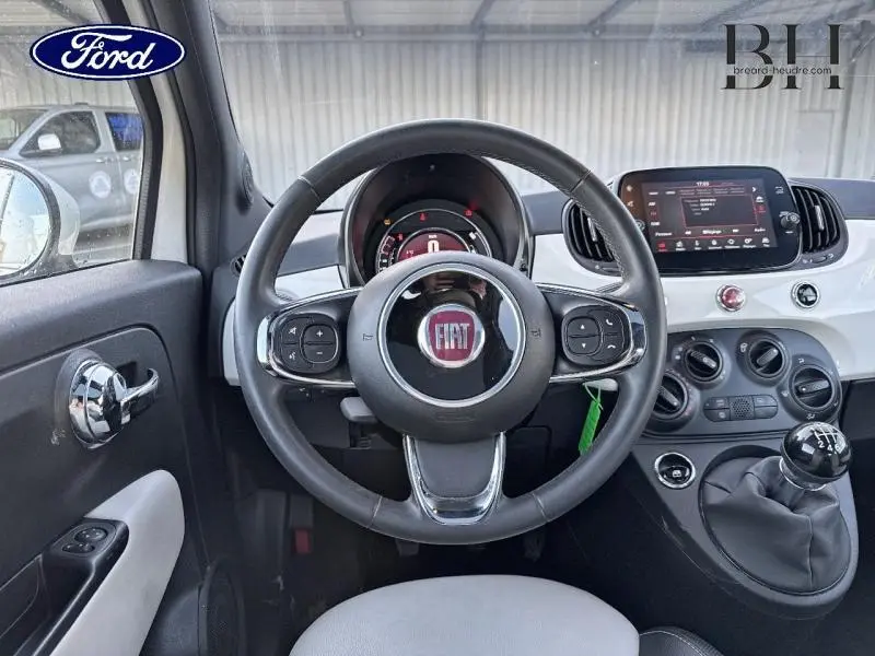 Vue intérieure centrée sur le volant cuir multifonction et la console blanche brillante d'une Fiat 500 Bossa Nova White Pastel.