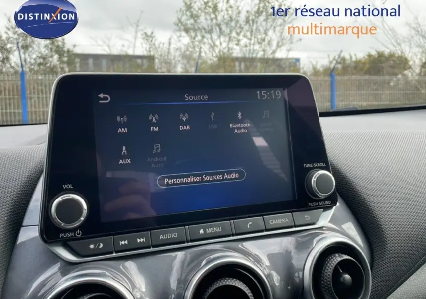 Écran tactile central du Nissan Juke 2023 en noir perle métal, avec commandes audio et ventilation visibles.