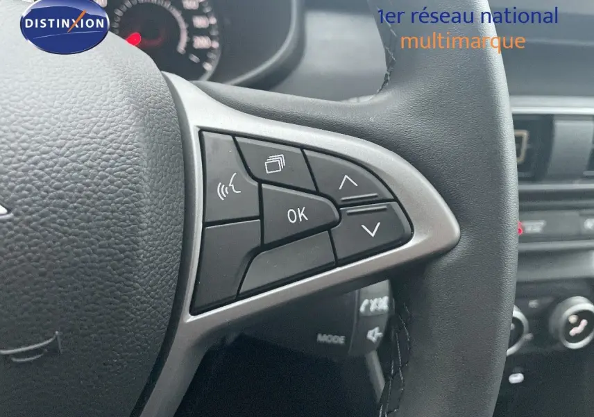 Gros plan sur le volant noir avec commandes multifonctions du Dacia Jogger gris schiste, tableau de bord en arrière-plan.