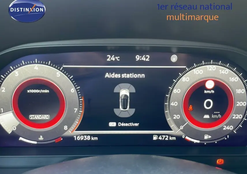 Tableau de bord numérique du Nissan Juke noir, affichant les aides au stationnement et compteurs à aiguille rouges.