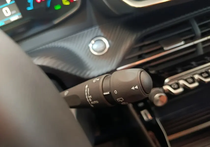 Gros plan sur la commande d’essuie-glace à gauche du volant dans l’habitacle noir du Peugeot E-2008 électrique gris clair.