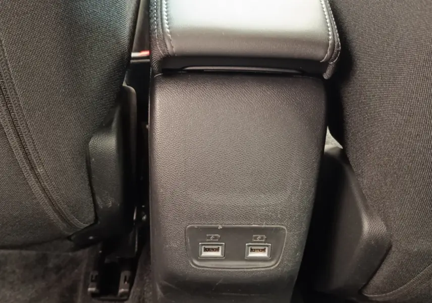 Gros plan sur la console centrale arrière noire avec deux ports USB entre les sièges tissu noirs du Peugeot E-2008 électrique.