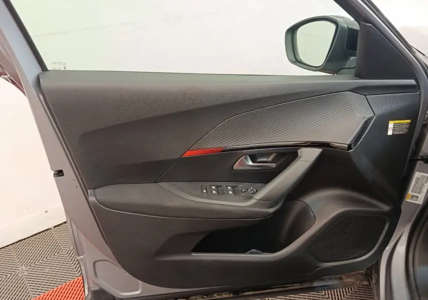 Vue intérieure de la porte avant gauche gris clair du Peugeot E-2008 électrique avec insert carbone et commandes fenêtres.