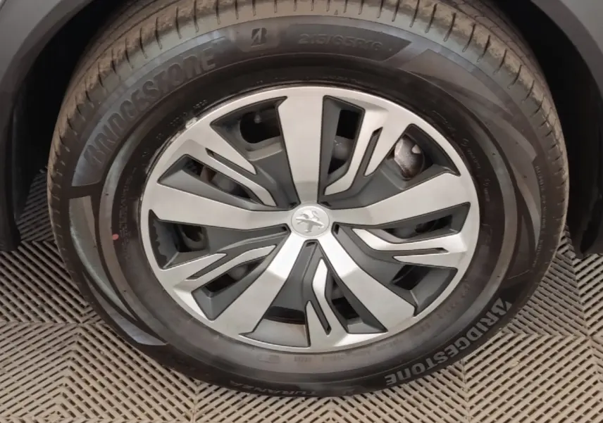 Gros plan sur la roue avant droite de la Peugeot E-2008 électrique gris clair avec jante alliage et logo lion central.
