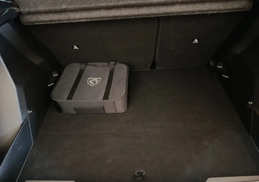 Coffre spacieux de Peugeot E-2008 électrique gris clair avec sac de rangement Peugeot posé au sol.