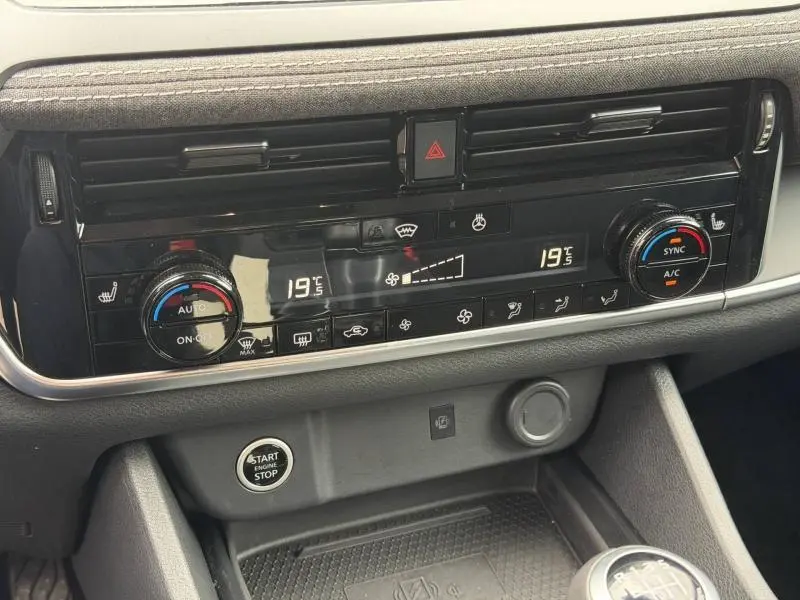 Gros plan sur la console centrale noire du Nissan Qashqai blanc nacré, affichant la climatisation digitale à 19°C.