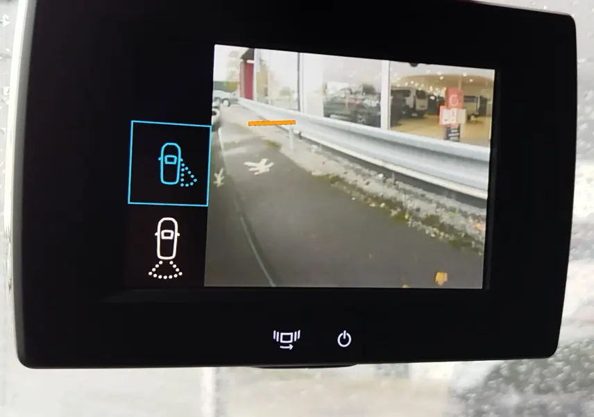 Écran de caméra de recul du Peugeot Partner 2020 montrant le côté droit gris foncé avec barrière de sécurité et bâtiment en arrière-plan.