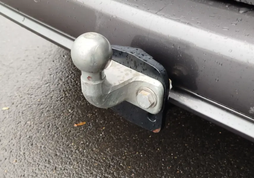 Gros plan sur la boule d'attelage métallique fixée à l'arrière d'un Peugeot Partner gris foncé sous la pluie.