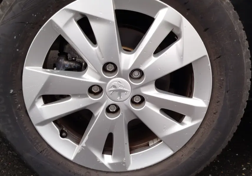 Gros plan sur la jante argentée avec logo Peugeot d’un pneu de Partner gris foncé, vue de face.