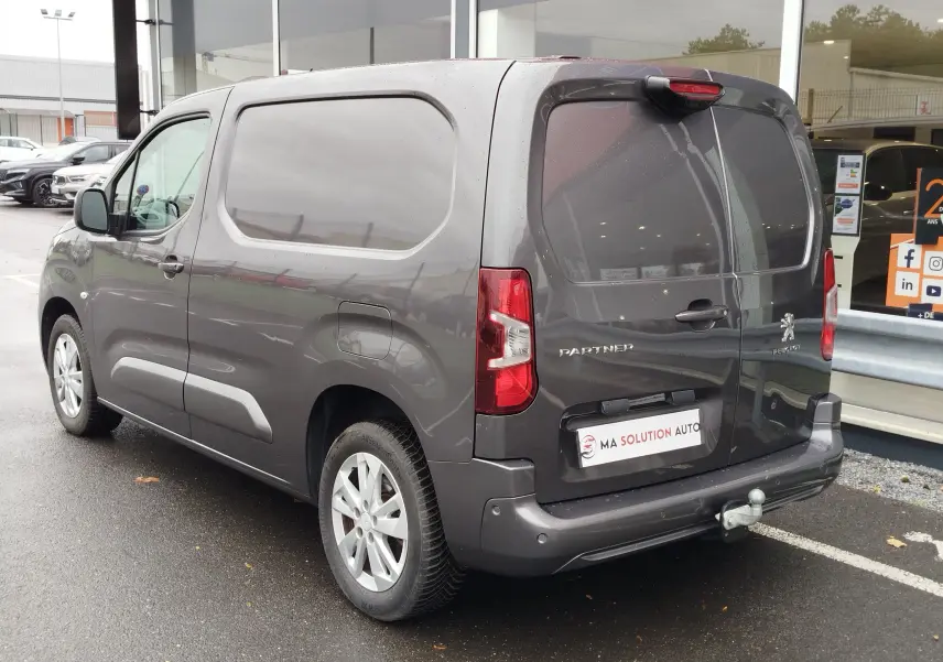 Vue 3/4 arrière droite d'un Peugeot Partner gris foncé 2020 avec hayon double porte et attelage de remorque.