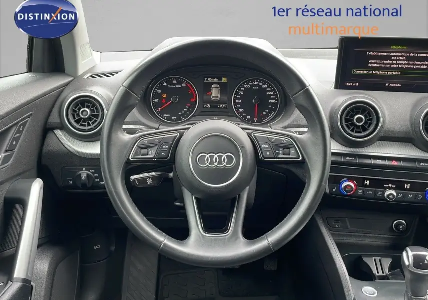 Vue frontale du poste de conduite de l'Audi Q2 noir mito metal 2023 avec volant multifonction et tableau de bord digital.