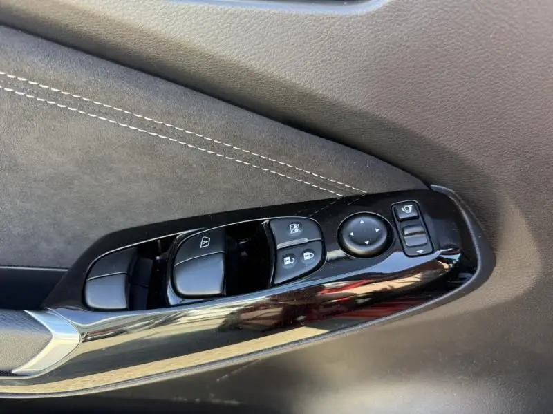 Gros plan sur les commandes de lève-vitres et rétroviseurs côté conducteur du Nissan Juke 1.6 Hybrid rouge Fuji métal avec toit noir.