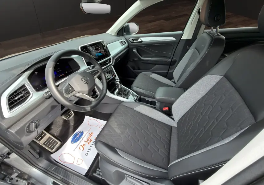 Vue intérieure côté conducteur du Volkswagen T-Roc 2025 avec sièges bi-matière gris et noir et tableau de bord moderne.