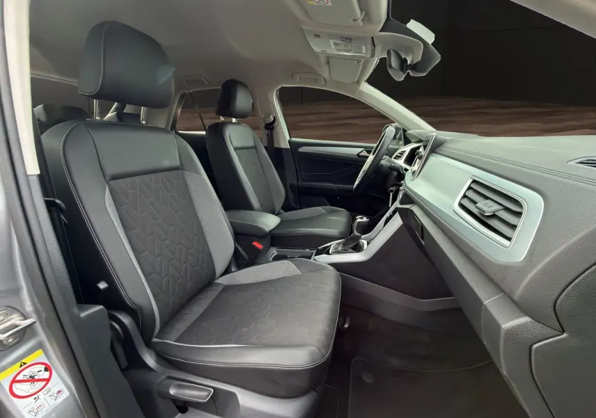 Vue intérieure côté gauche du Volkswagen T-Roc 2025, sièges tissu et cuir noirs avec console centrale et tableau de bord gris.