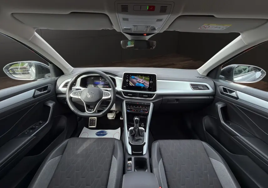 Vue intérieure avant du Volkswagen T-Roc 2025, tableau de bord noir avec écran tactile et volant multifonction cuir.