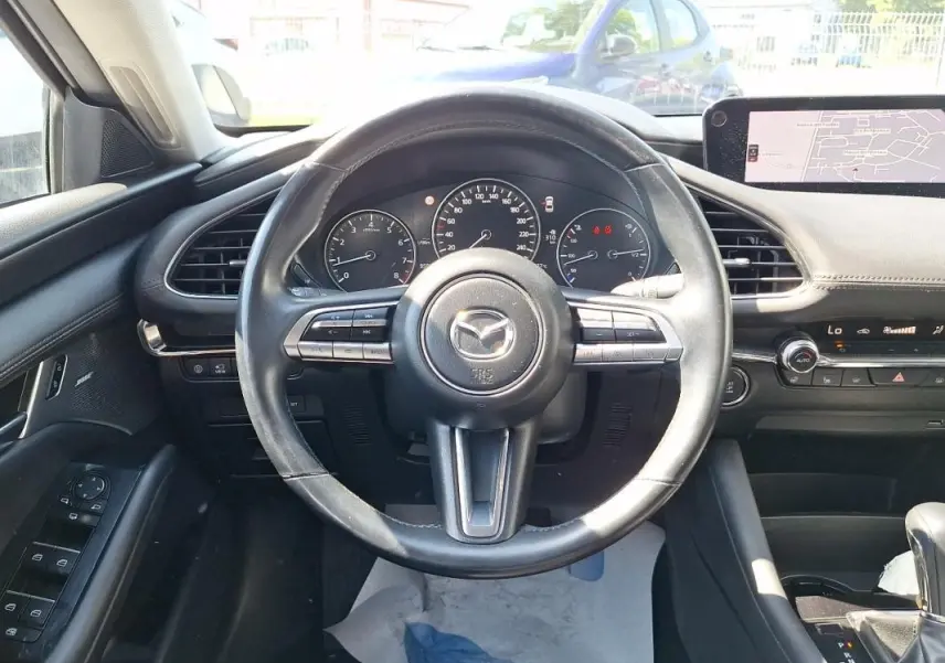 Vue intérieure centrée sur le volant cuir multifonctions d'une Mazda3 gris, avec tableau de bord et écran GPS visibles.