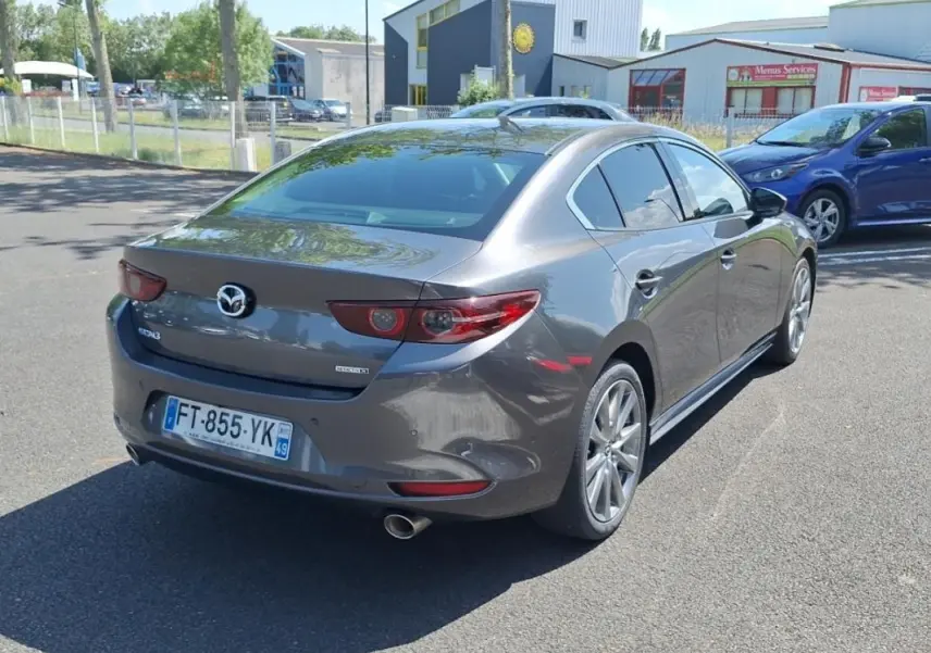 Vue 3/4 arrière droite d'une Mazda3 gris métallisé avec jantes aluminium et feux arrière LED distinctifs.