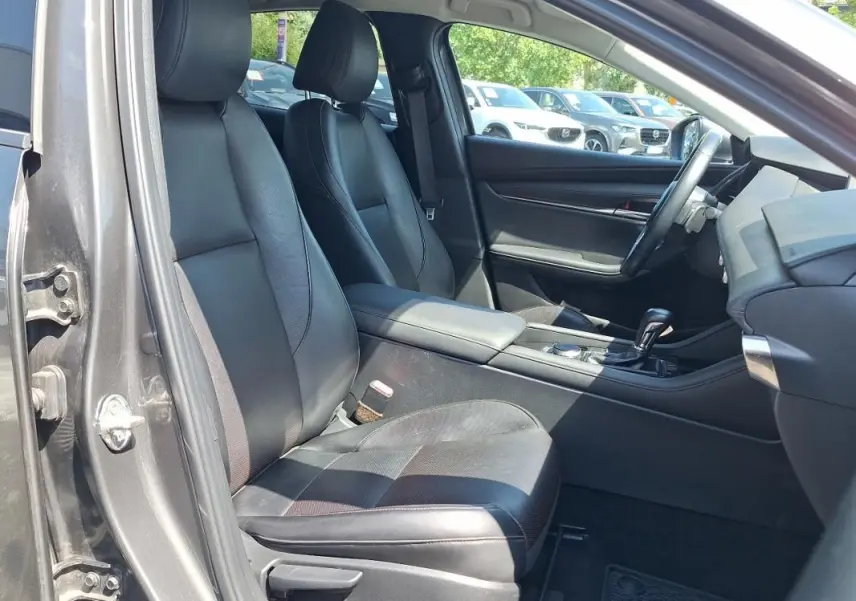 Vue intérieure côté conducteur de la Mazda3 gris, montrant sièges cuir noirs et console centrale avec levier de vitesse.