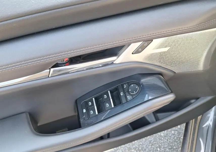 Gros plan sur la commande des vitres électriques et rétroviseurs sur la porte avant gauche grise d'une Mazda3.