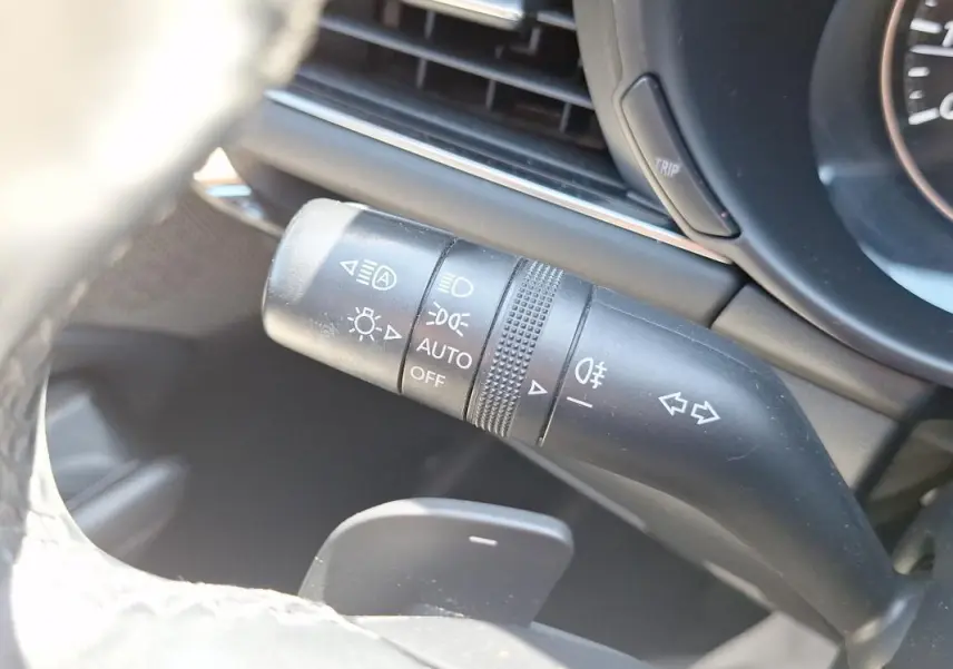 Gros plan sur la commande des phares et clignotants côté gauche du volant de la Mazda3 gris 2020.
