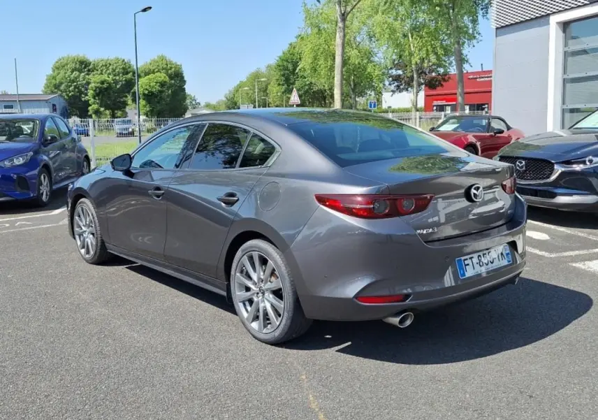 Vue 3/4 arrière droite d'une Mazda3 gris métallisé 2020 avec jantes aluminium et feux arrière LED distinctifs.