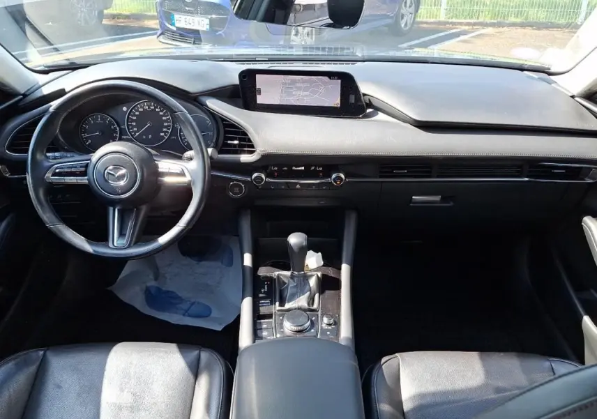 Vue intérieure avant de la Mazda3 2020 gris, mettant en valeur le volant cuir multifonctions et l’écran GPS central.