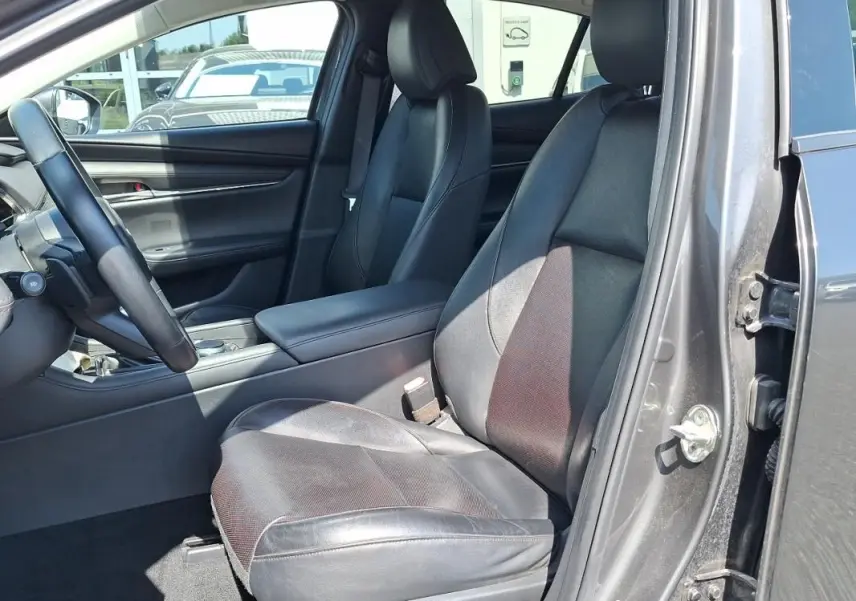 Vue intérieure côté conducteur de la Mazda3 gris 2020, sièges en cuir noir et volant multifonctions visible.