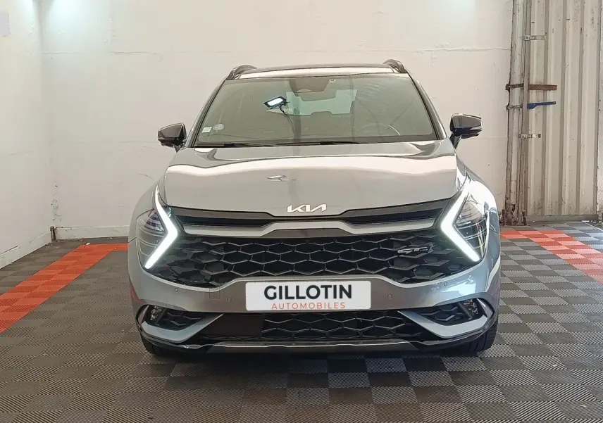 Vue frontale d'un KIA SPORTAGE gris clair 2022 avec feux LED en forme de flèche et calandre noire hexagonale.