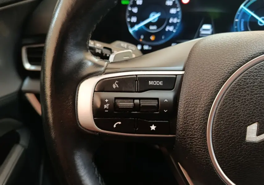 Gros plan sur les commandes gauche du volant cuir noir du Kia Sportage 2022 avec tableau de bord digital en arrière-plan.