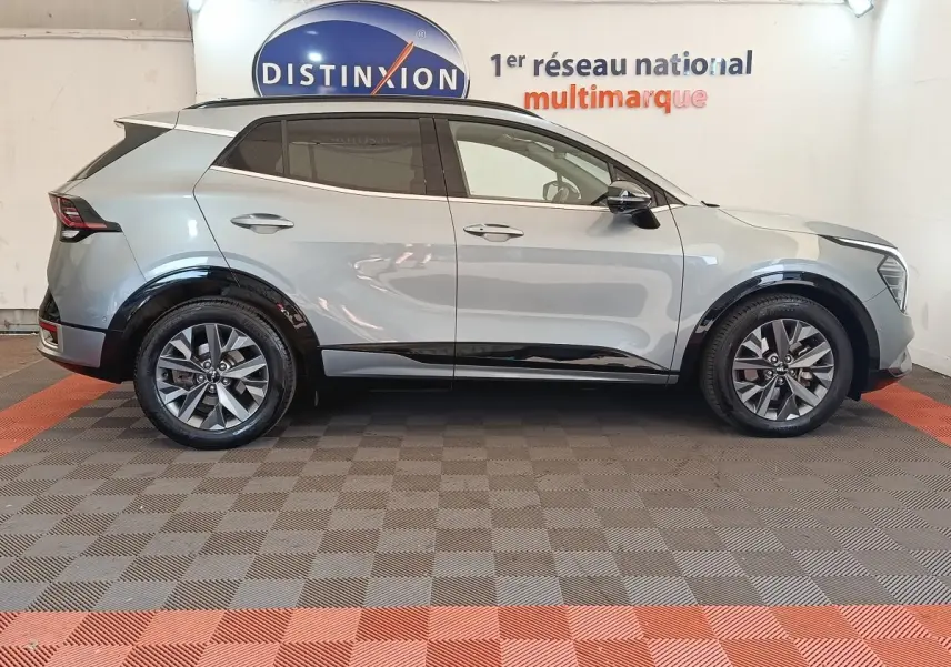 Profil droit d'un KIA SPORTAGE gris clair 2022 avec jantes alliage et rétroviseurs électriques dans un showroom.