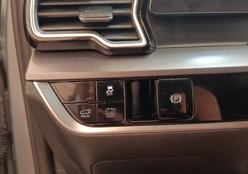 Gros plan sur les commandes noires du tableau de bord du Kia Sportage gris clair, avec boutons de frein à main et maintien de frein.