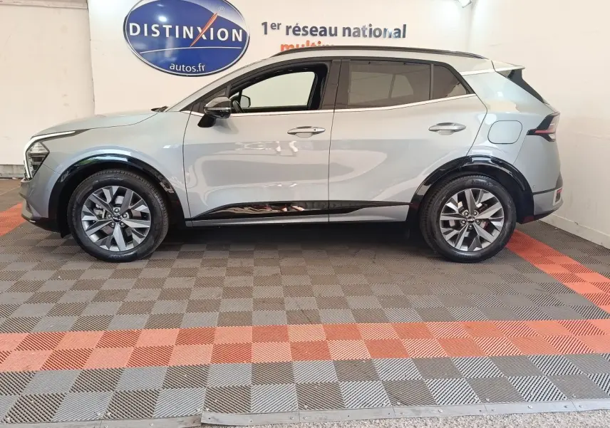 Vue latérale droite d'un KIA Sportage gris clair 2022 avec jantes alliage et protections noires sur passages de roues.