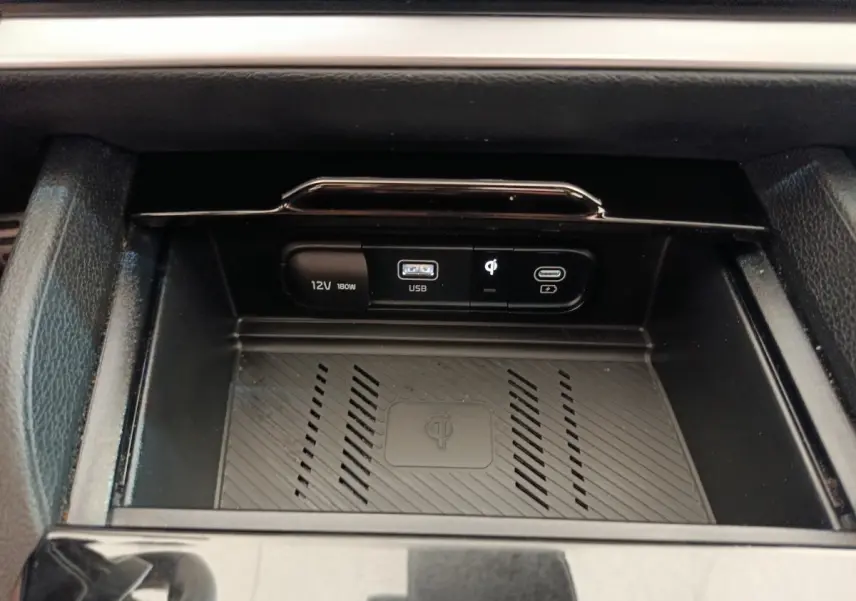 Gros plan sur la zone de recharge sans fil et ports USB 12V du Kia Sportage gris clair 2022, intérieur noir.