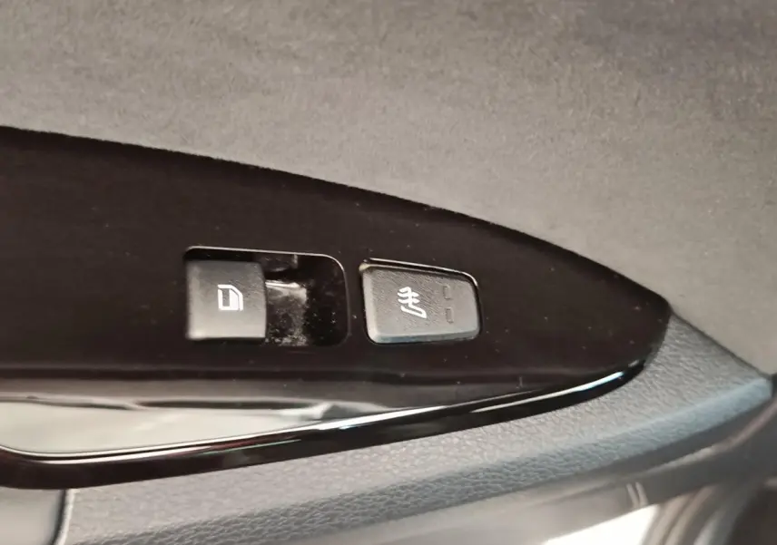 Gros plan sur les boutons de commande de verrouillage et de chauffage des sièges sur la porte intérieure noire d’un Kia Sportage gris clair.
