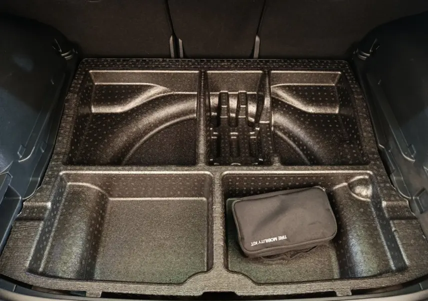 Coffre ouvert d’un Kia Sportage gris clair, vue plongeante sur le rangement compartimenté avec trousse de mobilité noire.