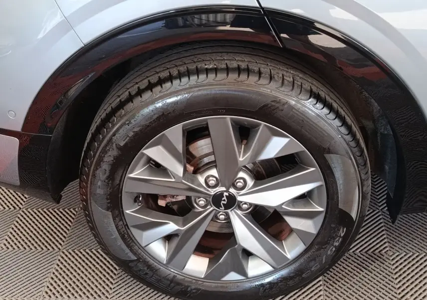 Gros plan sur la roue avant droite du KIA Sportage gris clair, avec jante alliage et logo KIA central visible.
