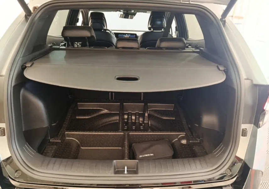 Coffre ouvert d’un KIA Sportage gris clair vu de l’arrière, avec cache-bagages et compartiments de rangement visibles.