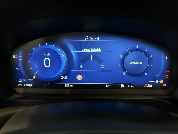 Tableau de bord numérique bleu du Ford Puma hybride 2022 affichant vitesse, régime moteur et jauge hybride.