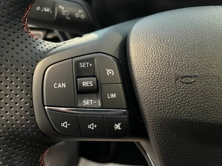 Gros plan sur les commandes de régulateur de vitesse et volume au volant perforé noir du Ford Puma blanc glacier 2022.