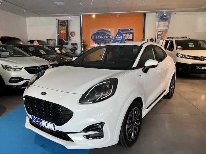 Ford Puma blanc glacier en 3/4 avant droit dans un showroom avec jantes noires et toit noir contrasté.