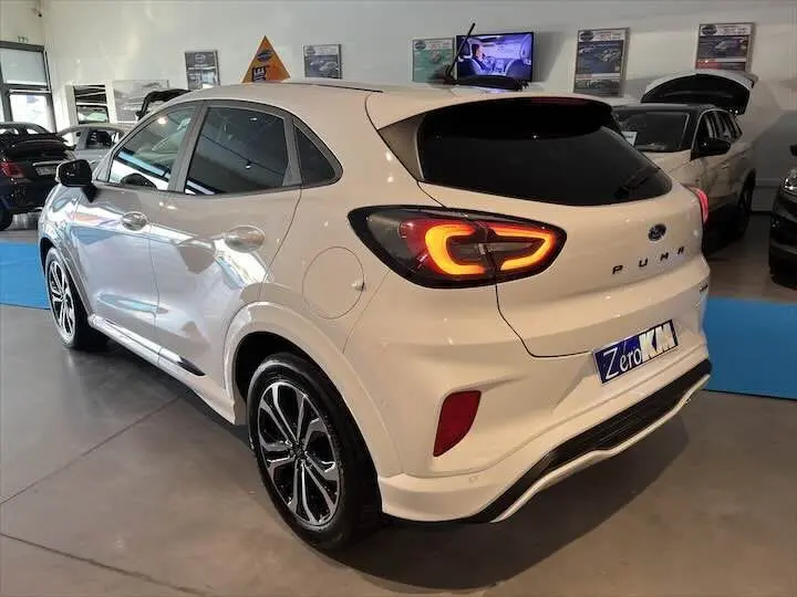 Ford Puma blanc glacier vu en 3/4 arrière droit dans un showroom, feux arrière allumés et jantes alliage noires.
