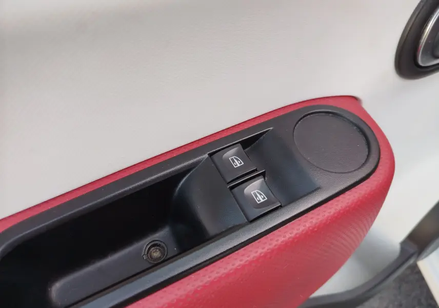 Détail de la commande des vitres électriques sur la porte intérieure droite rouge et blanche d'une Renault Twingo Blanc Cristal.
