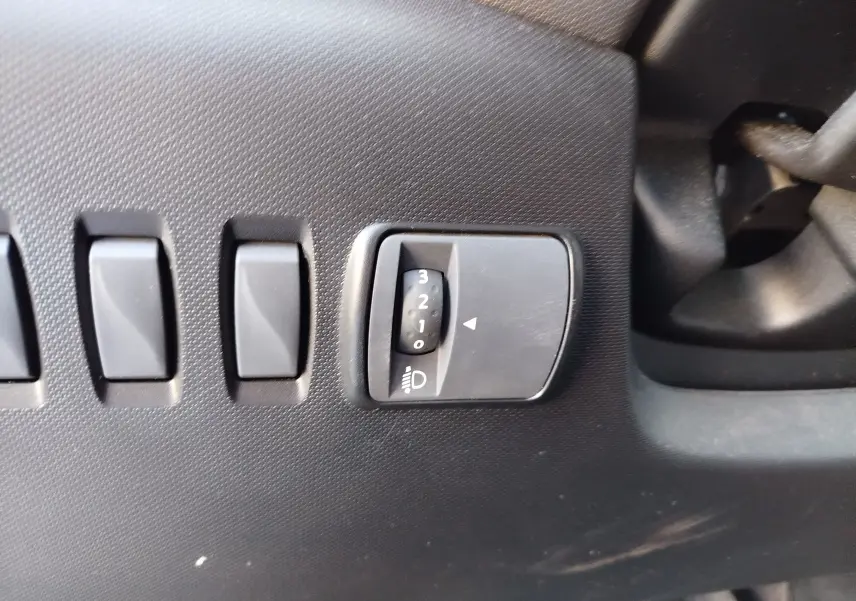 Gros plan sur le tableau de bord côté gauche de la Renault Twingo blanche, montrant les commandes de réglage des phares.
