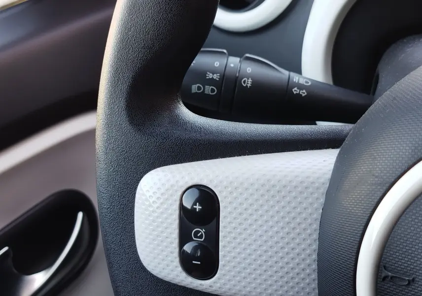 Gros plan sur la commande de régulateur de vitesse sur le volant noir et blanc d'une Renault Twingo Blanc Cristal 2016.
