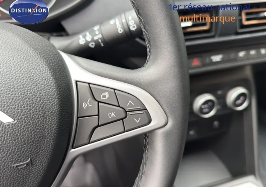 Gros plan sur le volant en cuir noir avec commandes intégrées, tableau de bord et commandes de climatisation floues en arrière-plan.