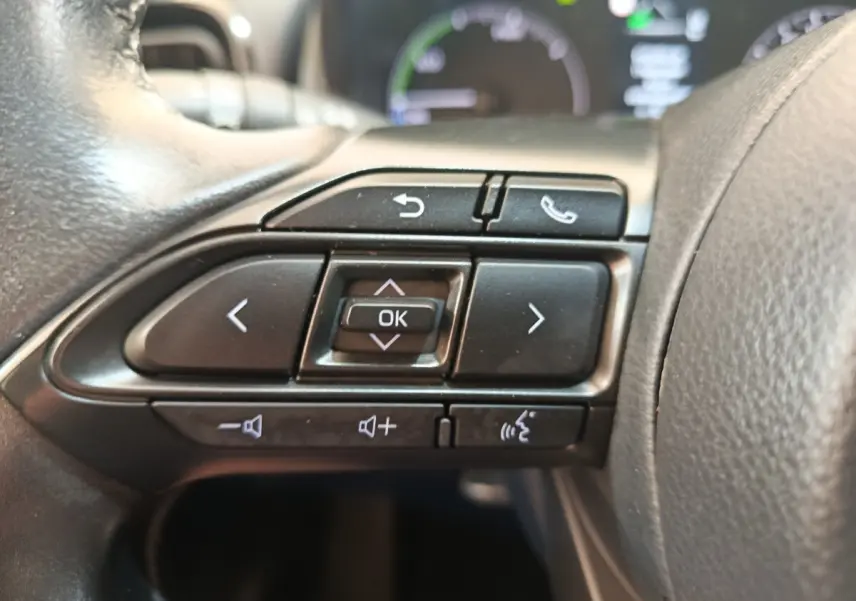 Gros plan sur les commandes multifonctions noires du volant cuir côté gauche de la Toyota Yaris hybride blanche 2022.